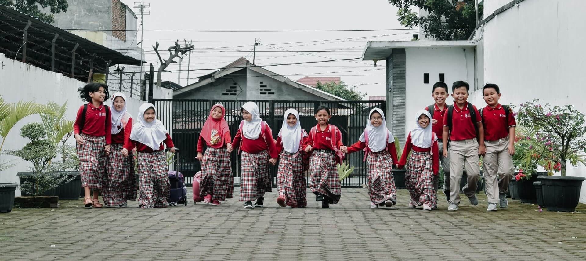 Siswa sekolah dasar berjalan bergandengan di halaman sekolah